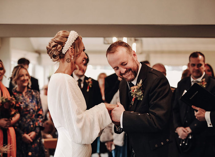 a groom laughing with his eyes closed while holding hands with bride wearing chunky pearl headband and textured ribbed wedding dress