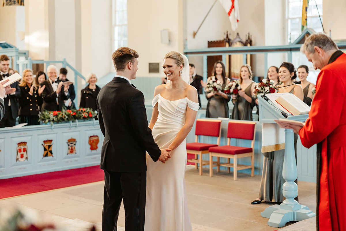 Bride and groom holding hands at the altar in Canongate Kirk as guests applaud behind them.