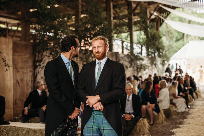 Two Men Wearing Tartan Trousers And Ties in front of wedding guests sitting on hay bales