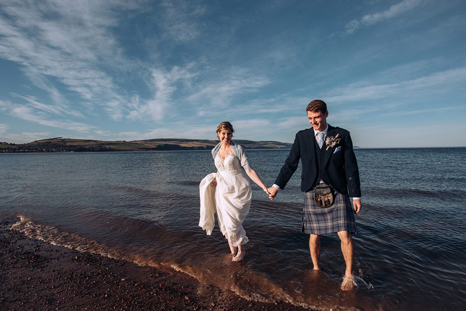 Bride and groom paddling in the sea wearing their wedding attire and laughing