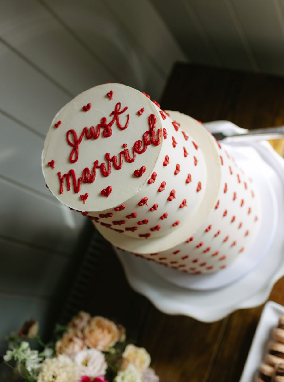 a white wedding cake with red piped love heart decor and 'just married' on top