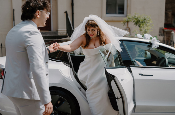 Bride is helped out of white wedding car