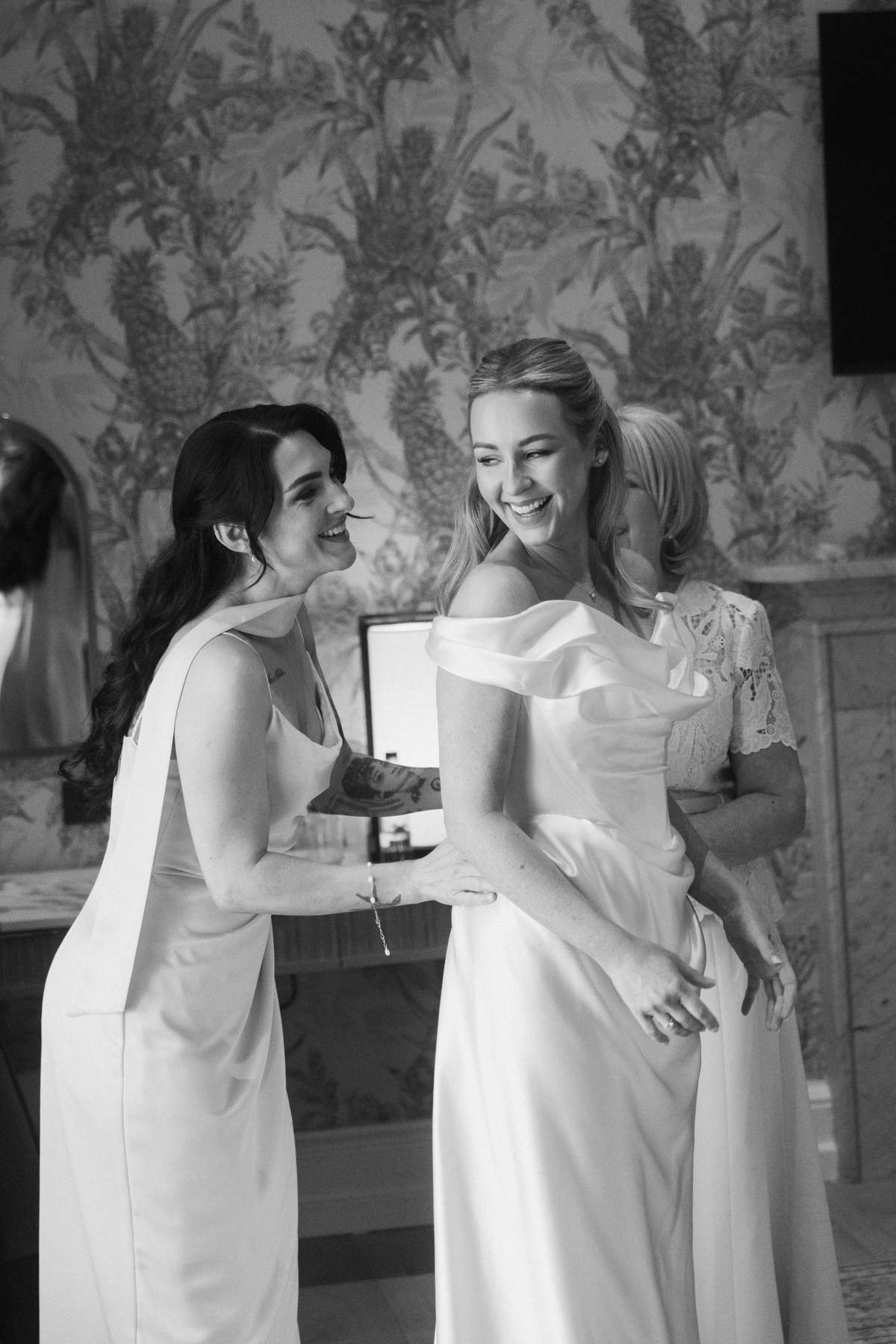 Siân laughs with her bridesmaid while getting into her Vivienne Westwood wedding dress before her Mar Hall ceremony.