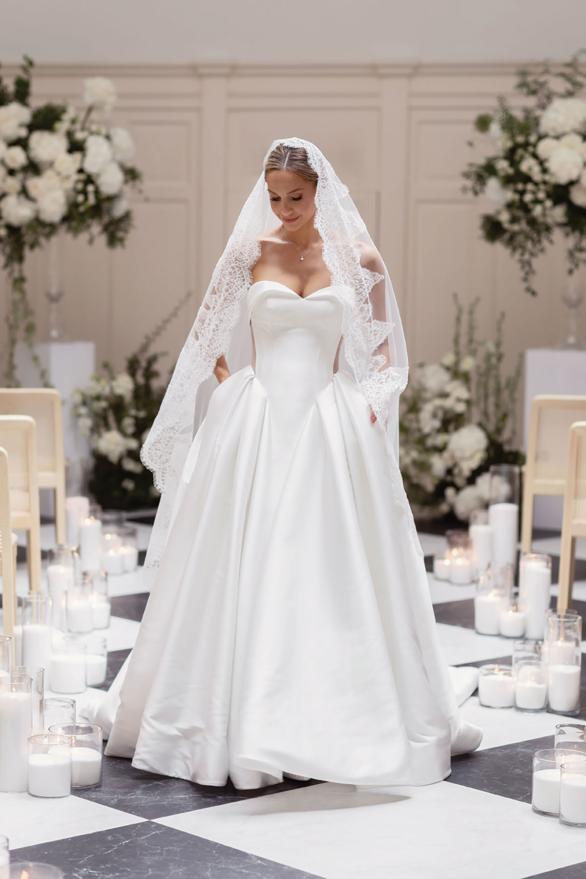 Bride in strapless ballgown with cathedral veil walking through candlelit aisle