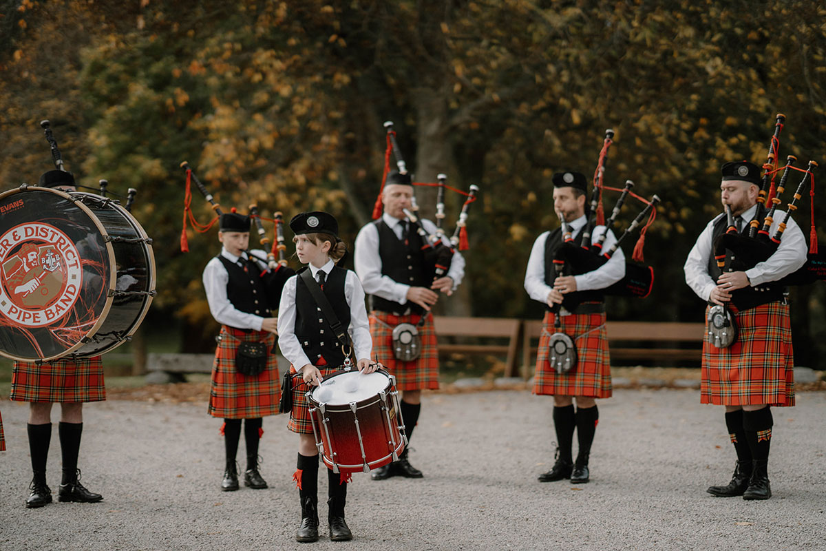 Scottish pipe band performing outdoors at Cluny Castle during an autumn wedding in Aberdeenshire.