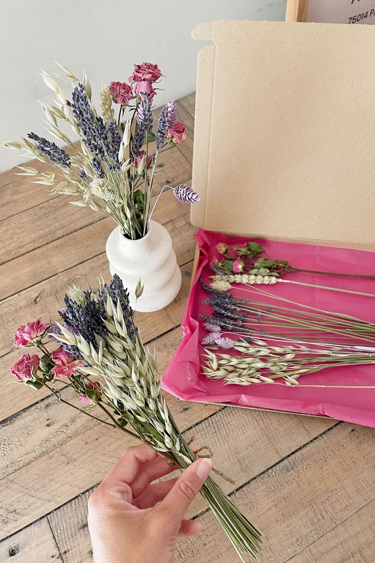 Dried flower delivery box with lavender, pink roses and oat stems arranged on a wooden table