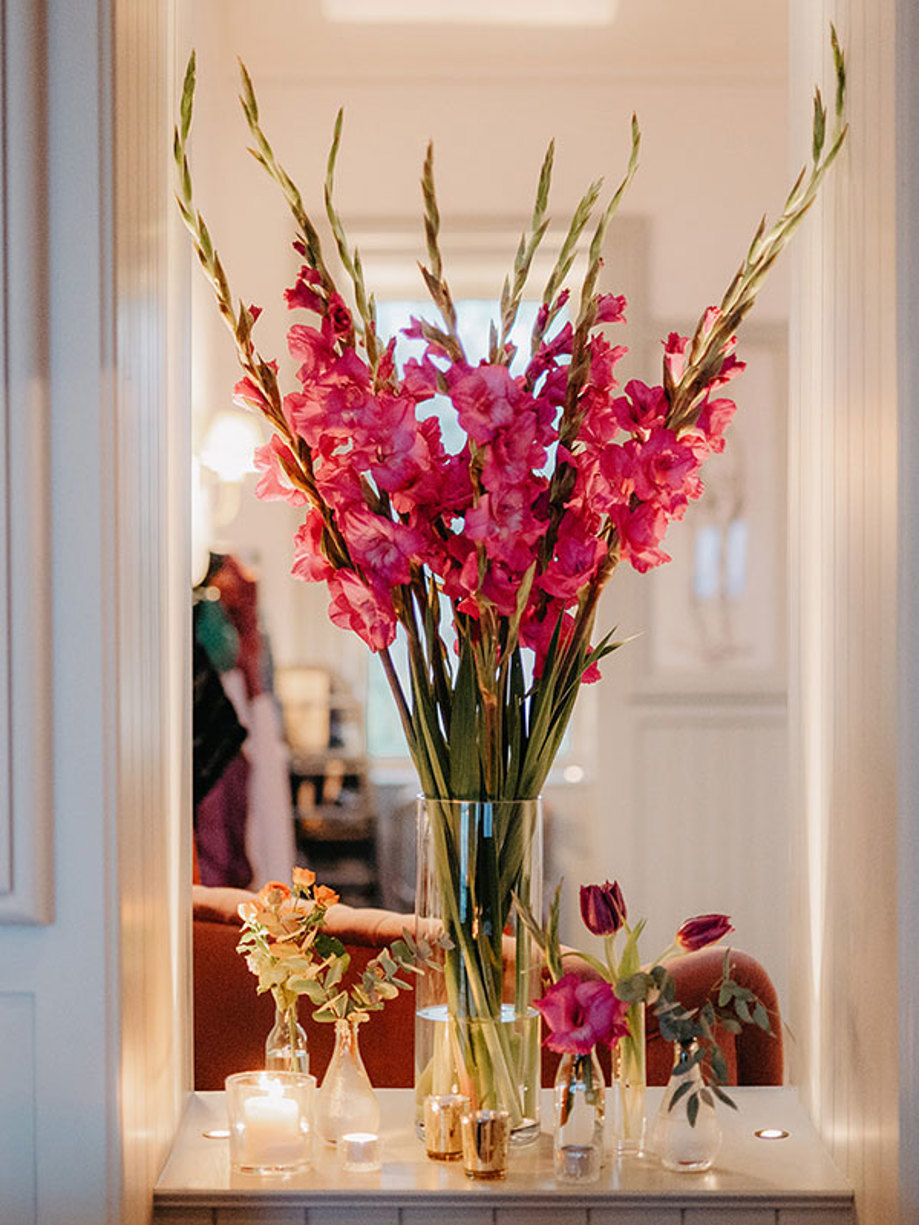 tall vase display of long stemmed pink flowers with small bud vases and candles scattered around it