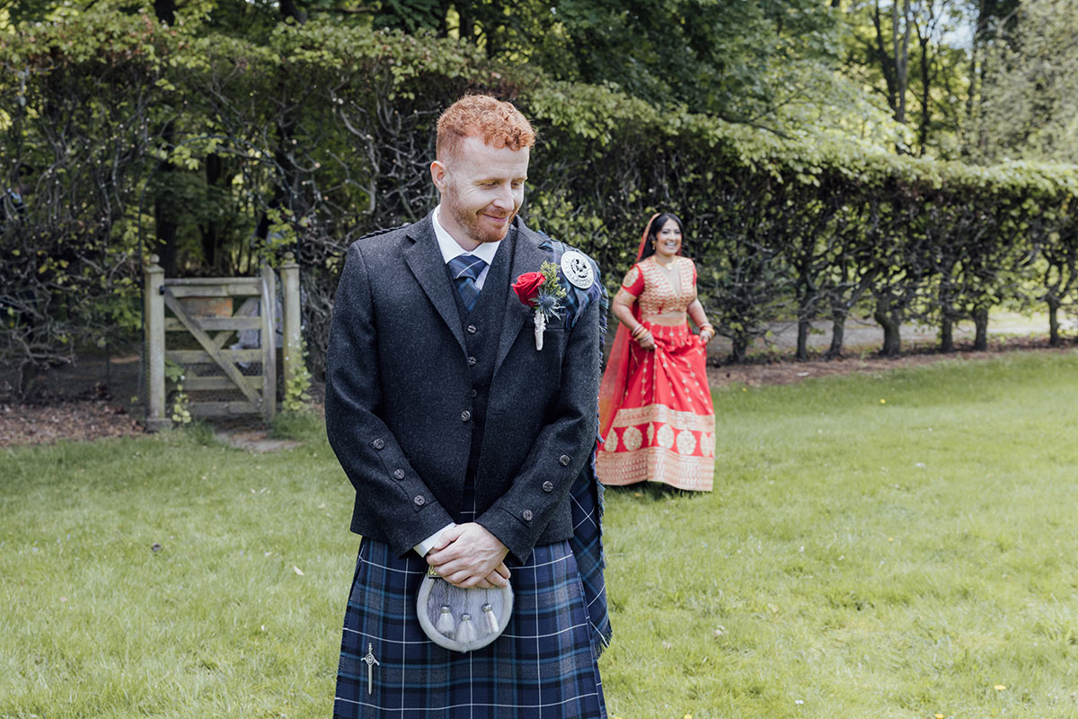 Scottish groom in a kilt smiling during a first look with his bride wearing a red Indian wedding dress at Atholl Palace Hotel