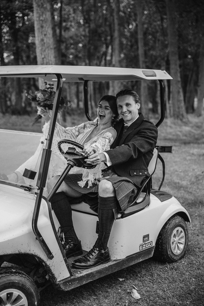 black and white image of bride and groom sat laughing in a golf buggy 