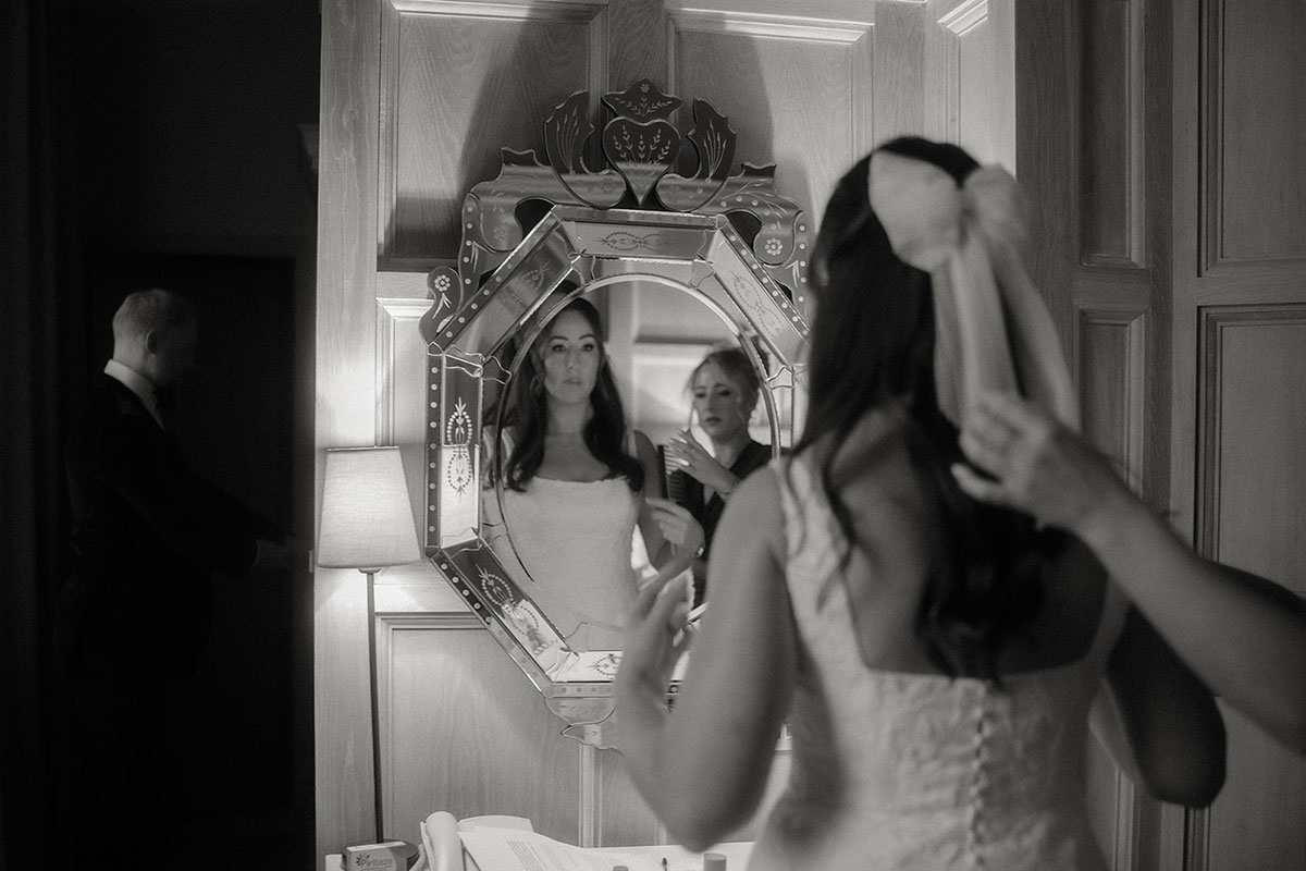 a bride looking in a mirror as someone fixes her hair