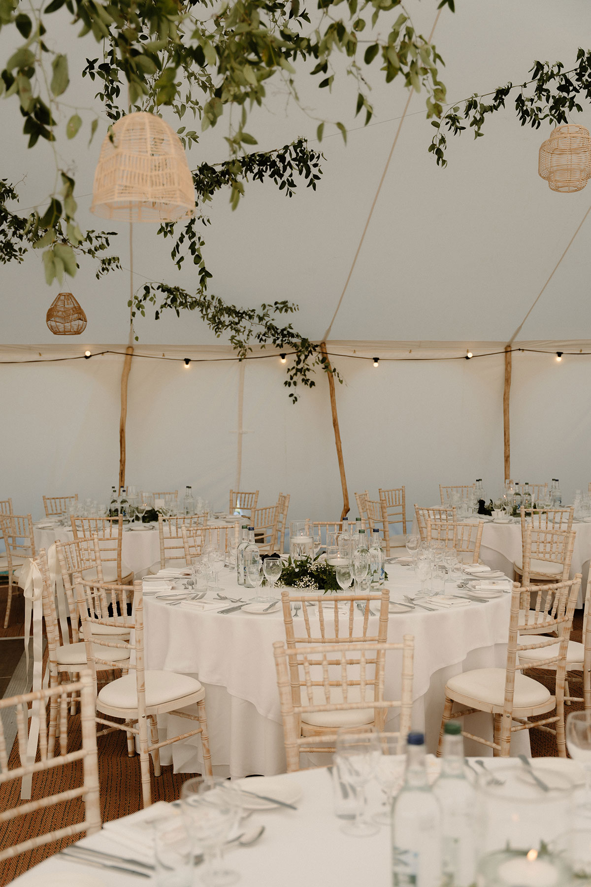 Inside a sailcloth wedding marquee with round reception tables, greenery installations and relaxed neutral wedding décor