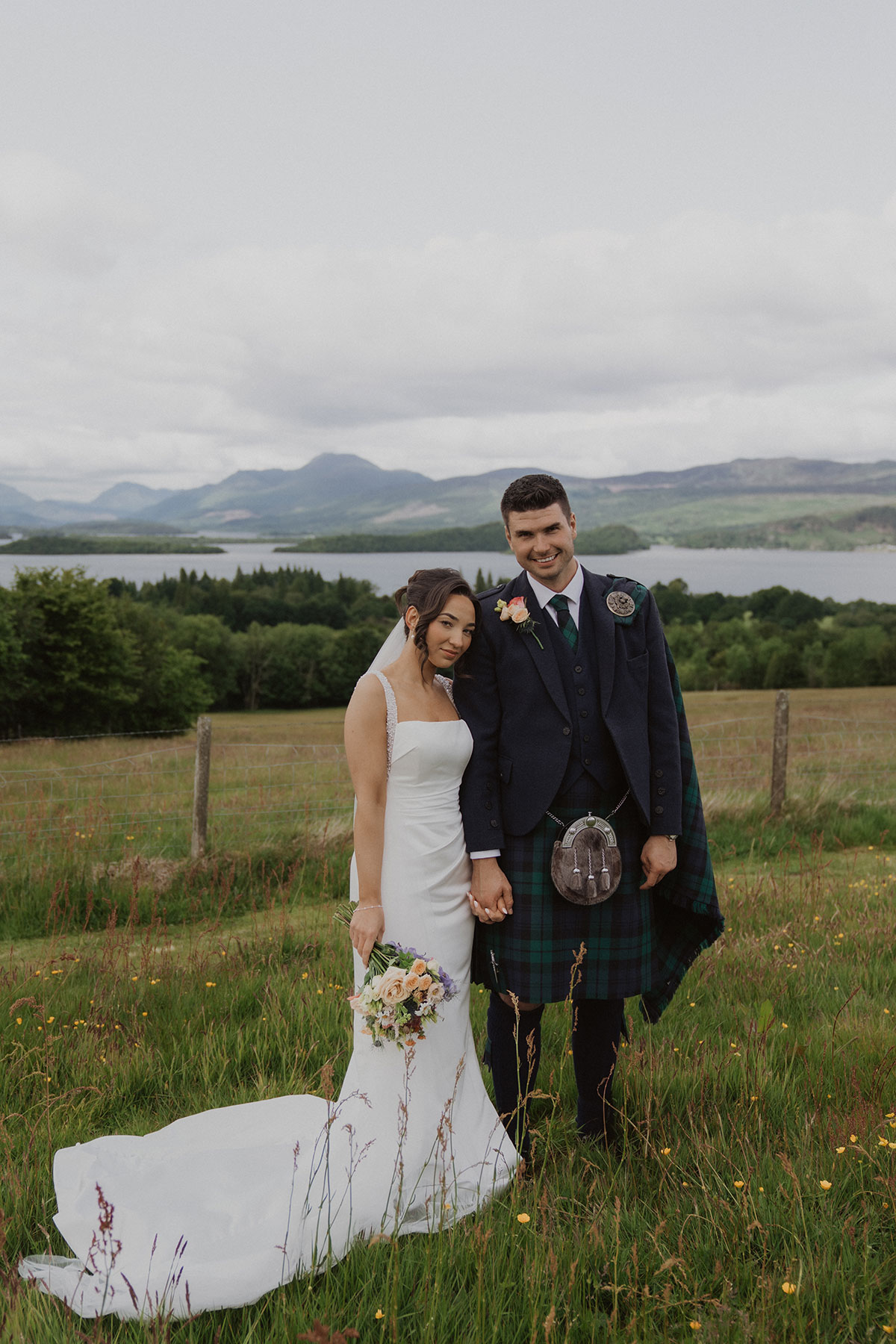 Scottish bride and groom portrait in grassy field with panoramic loch and mountain backdrop