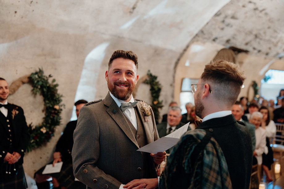 a groom looking emotional while reading from a folded sheet of paper during his wedding ceremony at Neidpath Castle