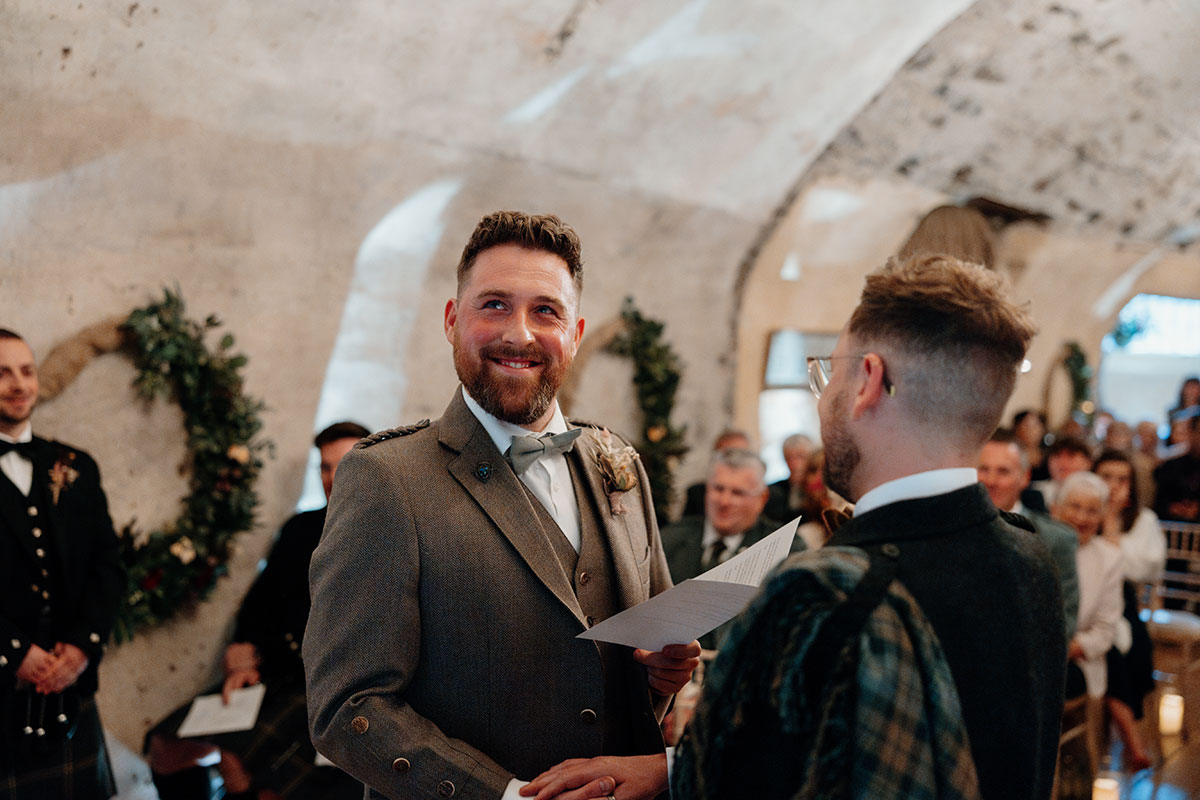 a groom looking emotional while reading from a folded sheet of paper during his wedding ceremony at Neidpath Castle