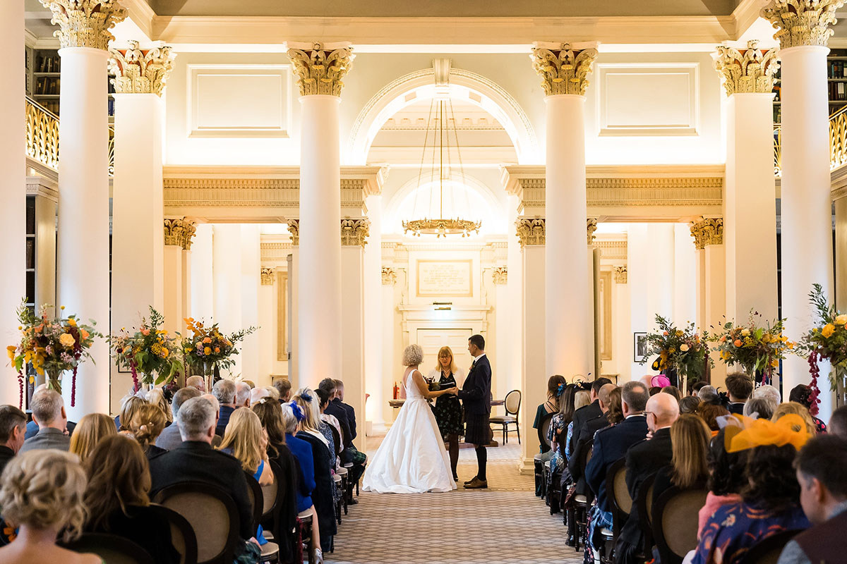 Wedding ceremony in the Lower Library at The Signet Library in Edinburgh with floral arrangements and neoclassical columns.