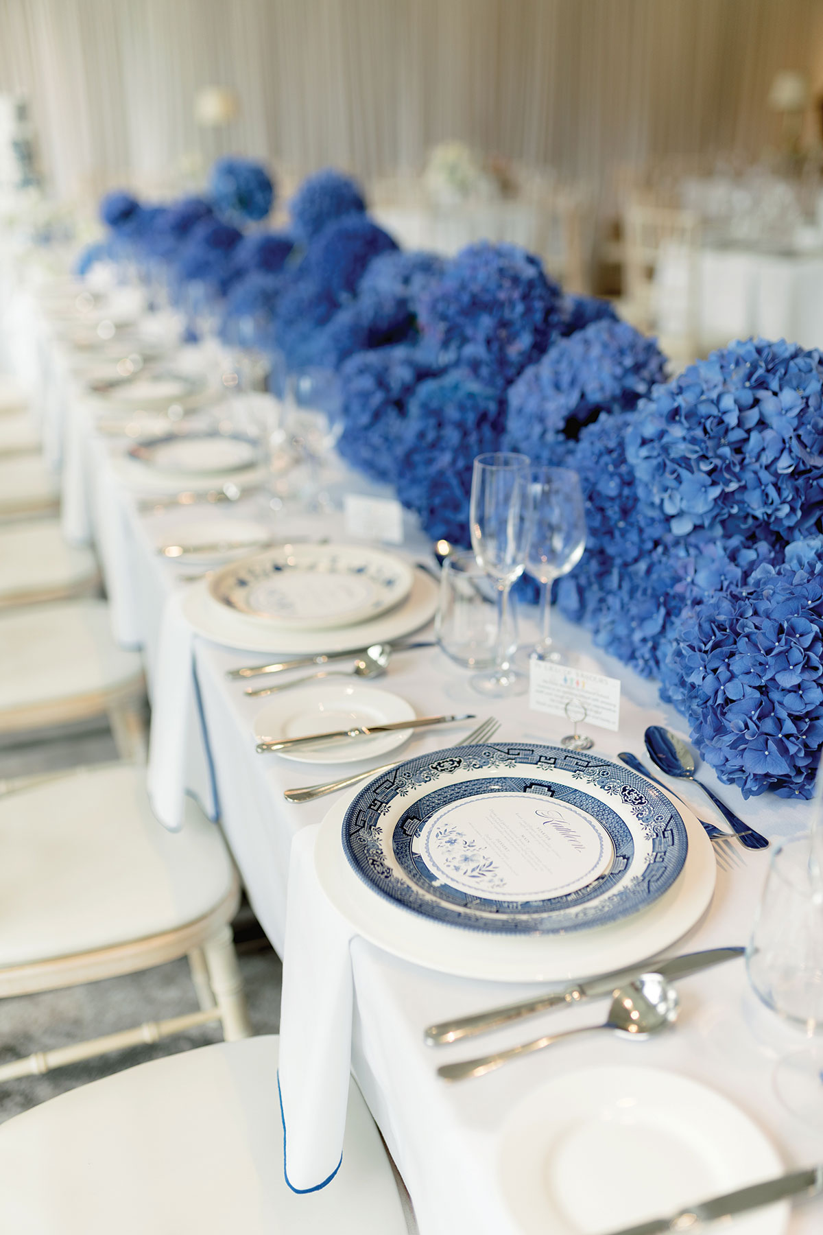 Wedding table decorated with vibrant blue hydrangea centrepieces and blue-and-white patterned plates arranged for a formal reception