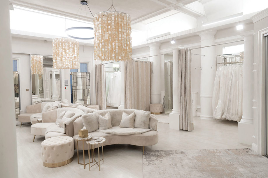 cream, beige and white decorated room with lots of mirrors, sofa seating and large curtained dressing rooms with large white hanging garment bags 