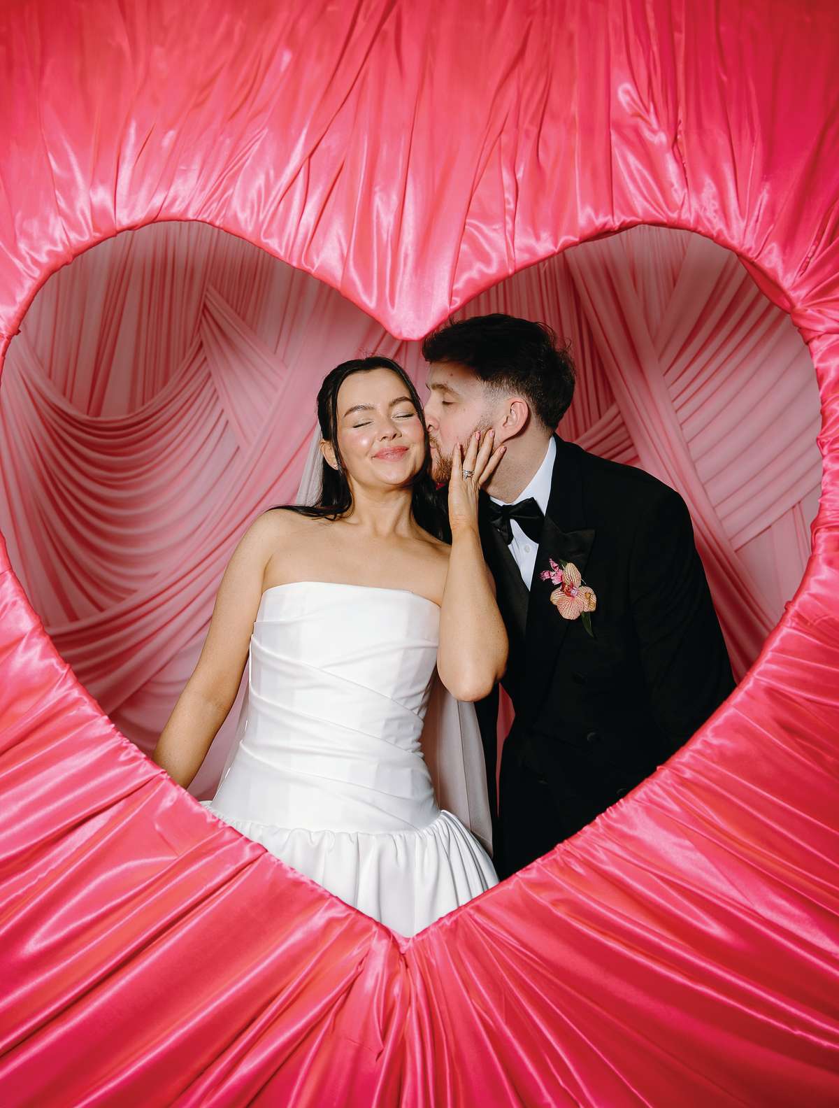 Newlyweds share a kiss inside a giant pink heart installation at their colourful wedding at The Collector’s Hall Glasgow.