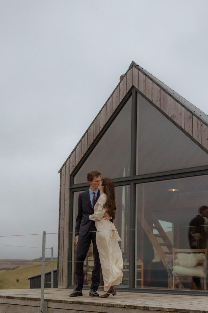 couple kiss in front of cabin with floor to ceiling windows