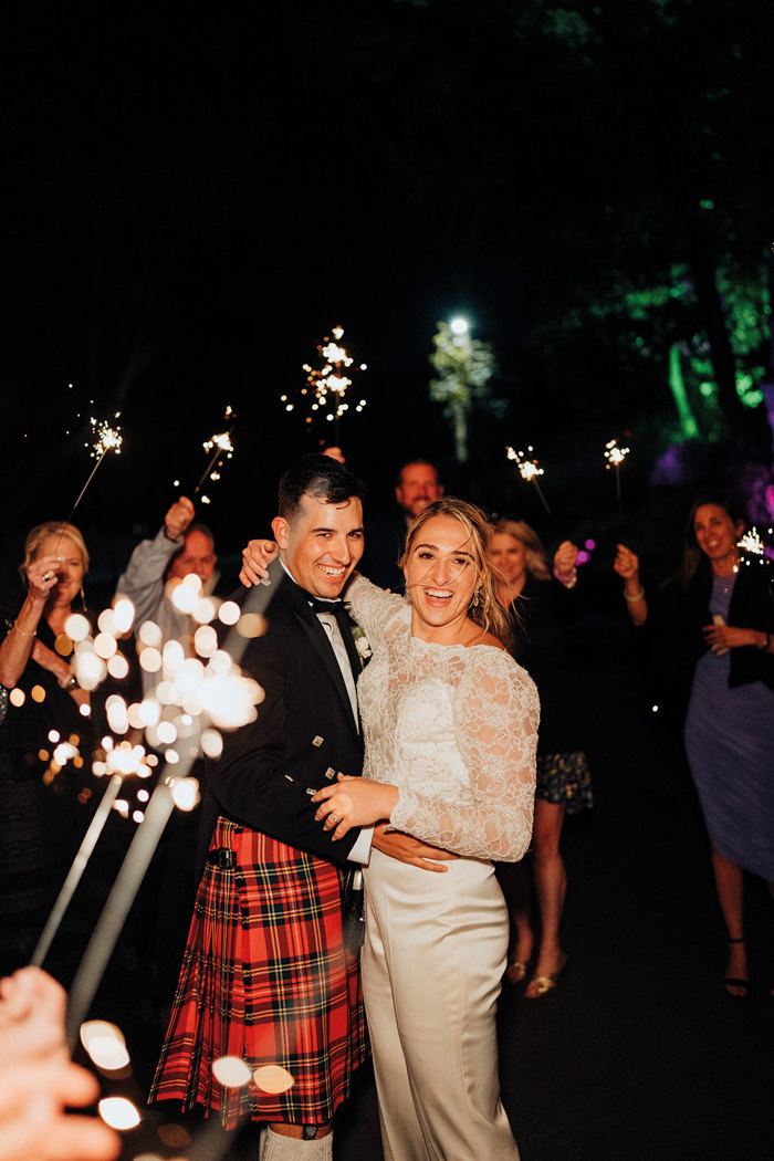 A bride and groom holding each other at nighttime surrounded by people holding sparklers.