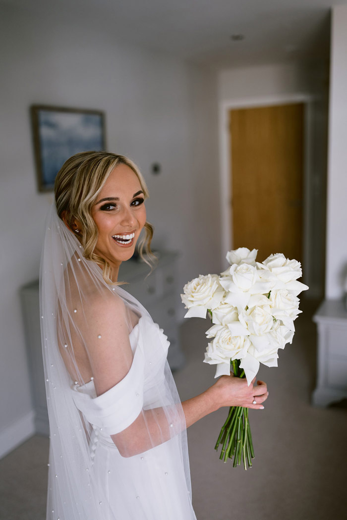 A person in a white dress holding a bouquet of white roses.