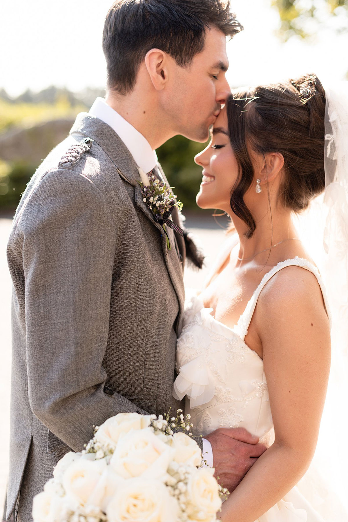 Groom kissing bride on the forehead in golden sunlight during romantic Old Course Hotel wedding portraits in St Andrews.