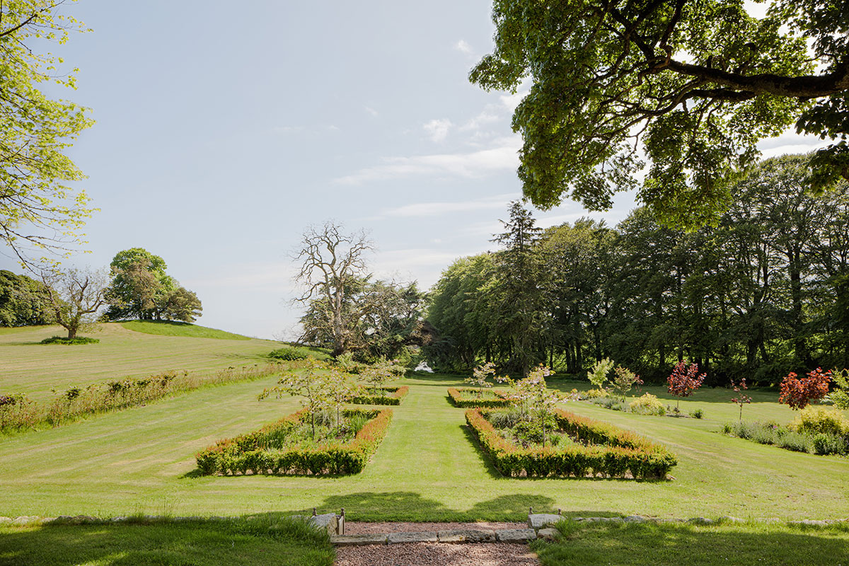 Landscaped gardens with manicured lawns, flowerbeds, and trees under a bright blue sky