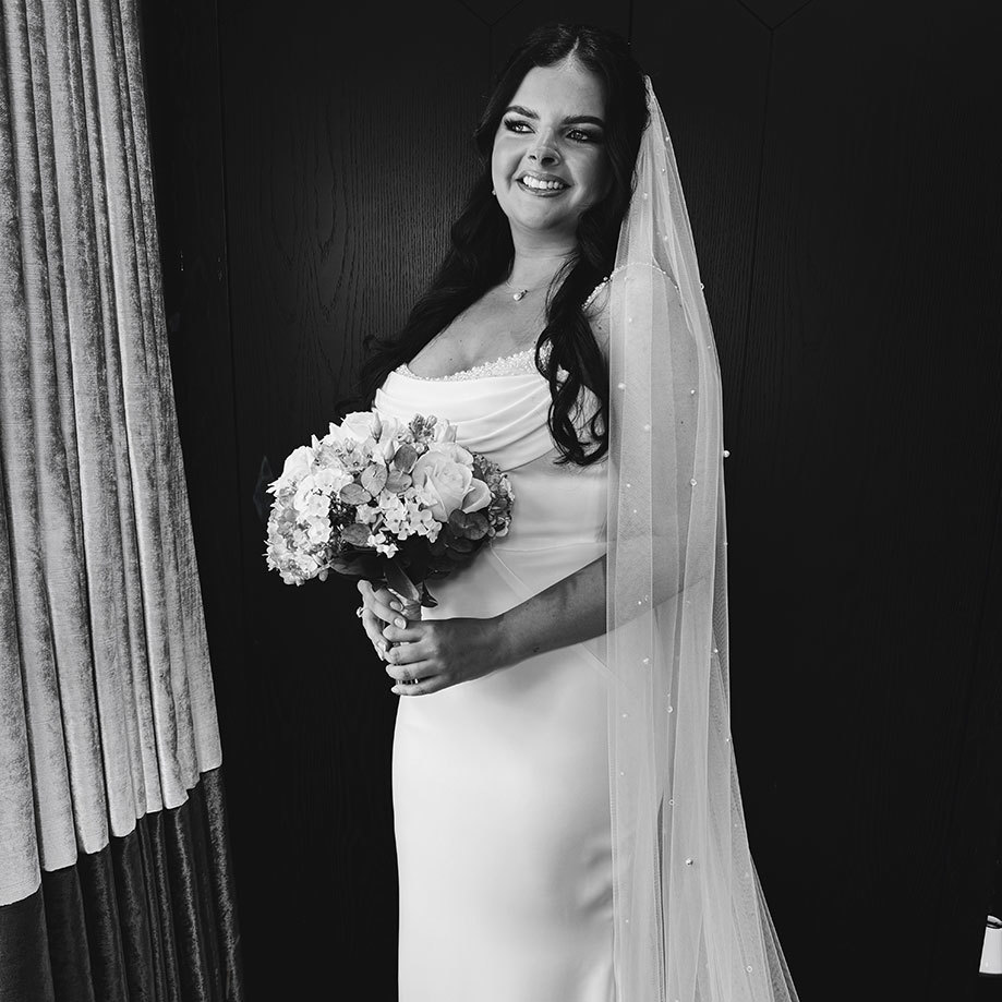 a smiling bride wearing a veil and holding a bouquet of flowers