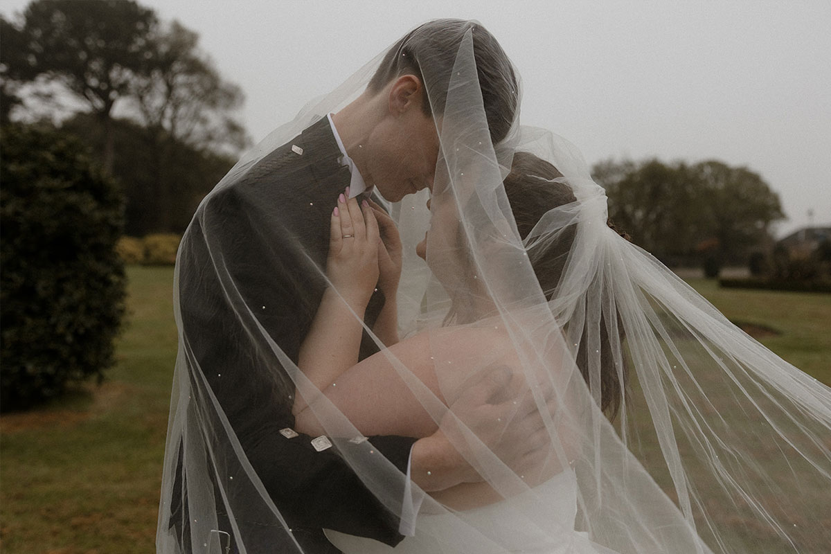 A couple stand together with their faces close to each other underneath a veil