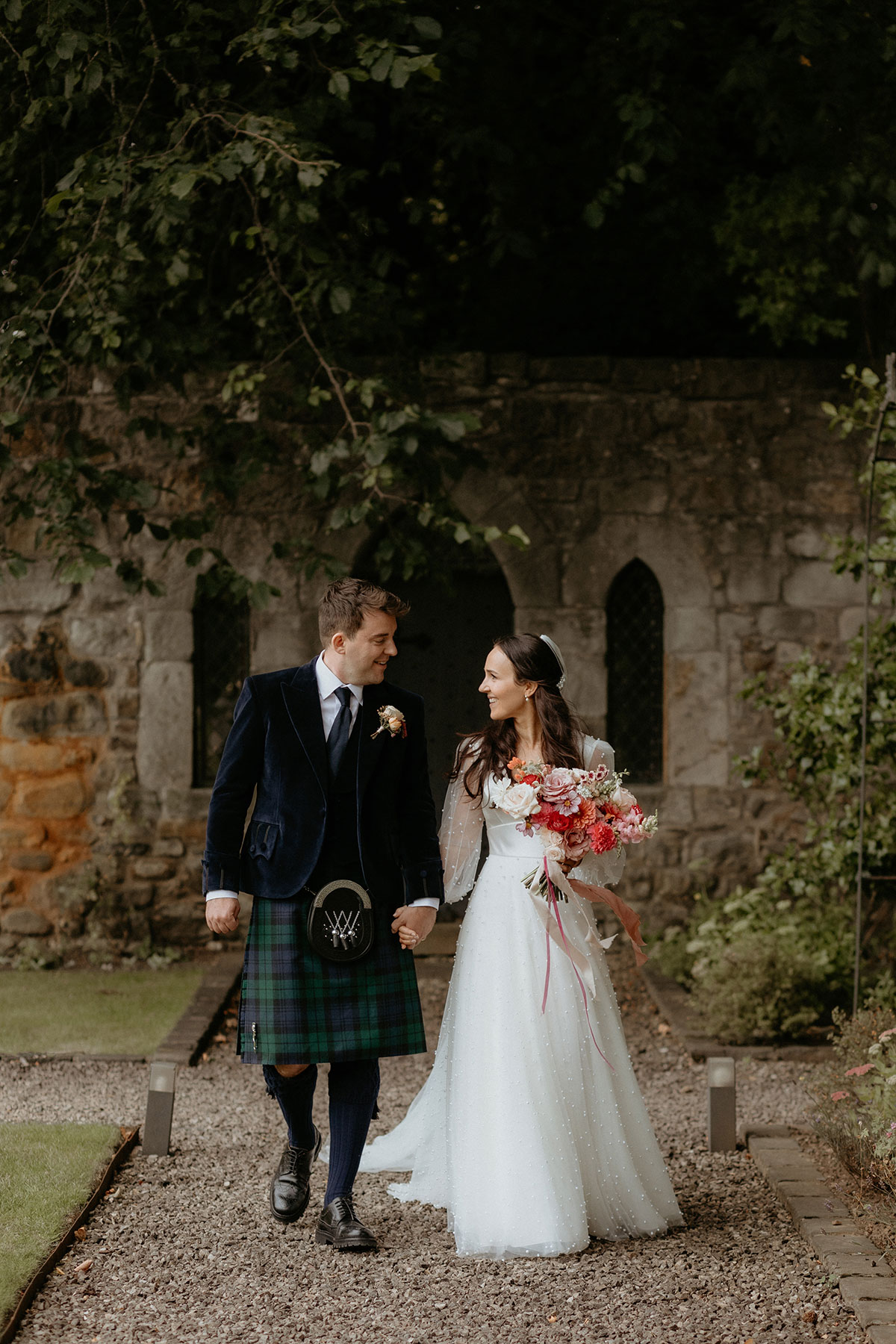 a bride and groom walking hand in hand through a garden at Carlowrie Castle