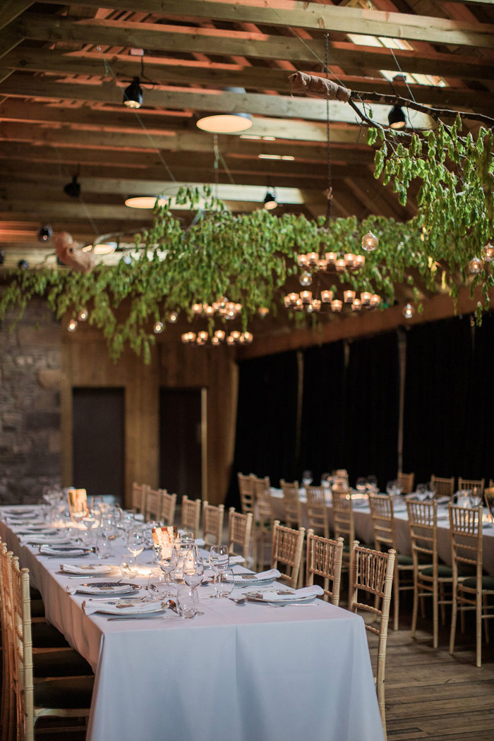 two long tables set for dinner with leaves decoration hanging from wooden beams at the Byre at Inchyra