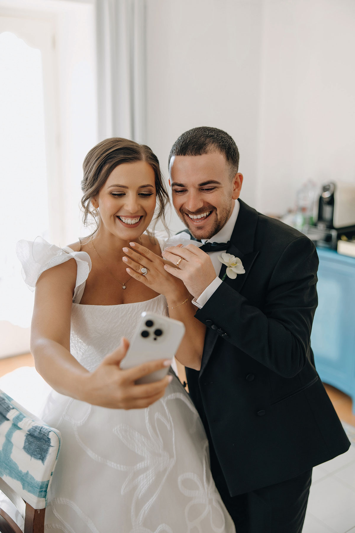 Wedding couple taking a selfie while showing their Tom Coll Jewellery engagement ring and wedding band