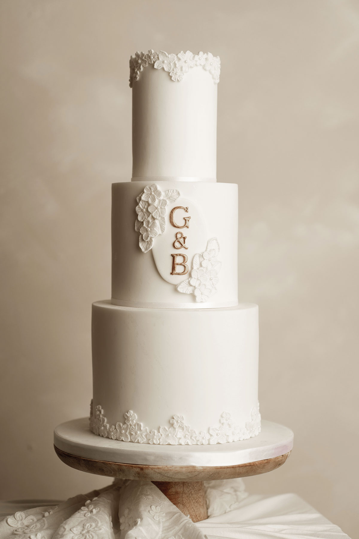 Modern white wedding cake with four tiers, delicate floral details and gold monogram initials “G & B”, created by Cakes by Nicole in Ayrshire