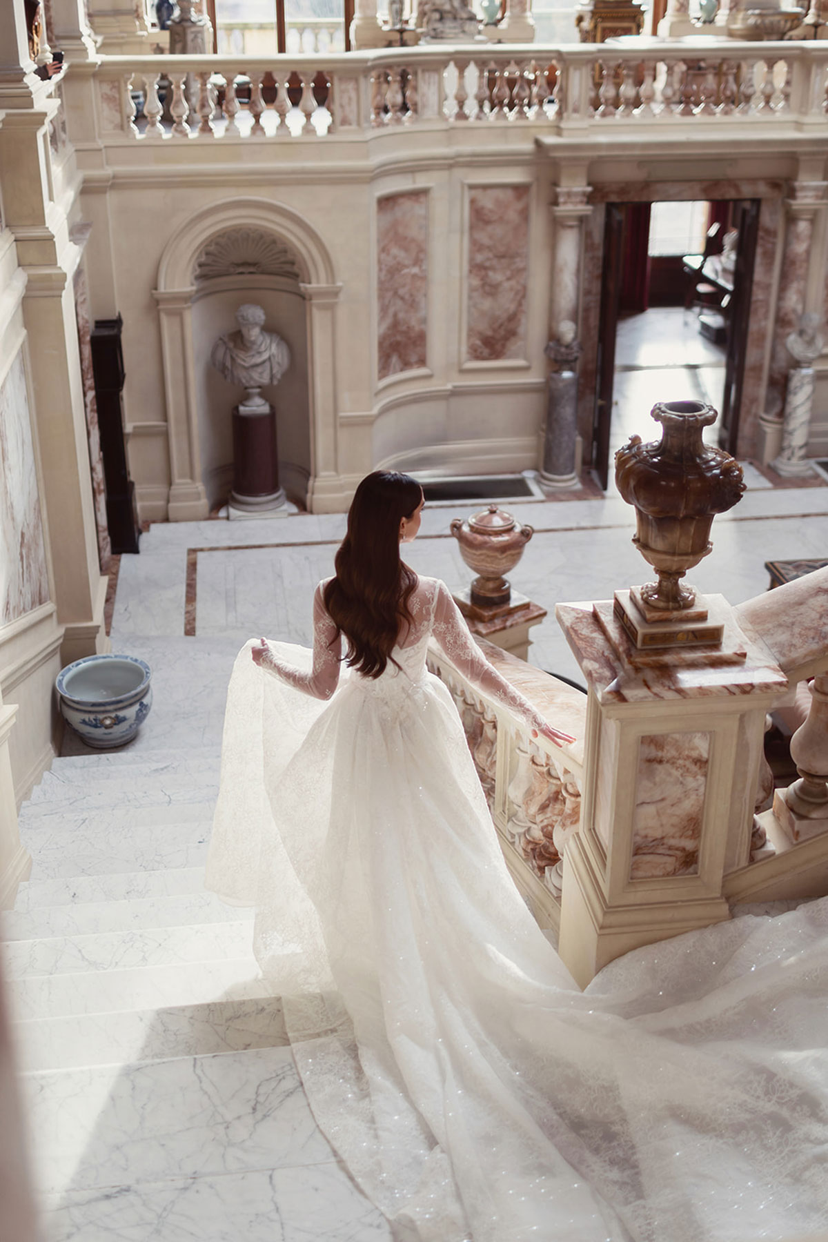 Bridal model in a lace-sleeved wedding dress descending the marble staircase at Gosford House.