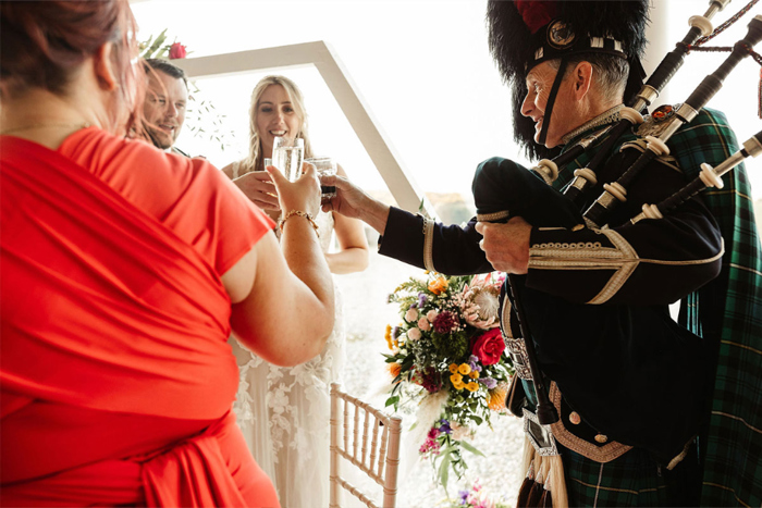 Bride and groom cheers their drink with piper