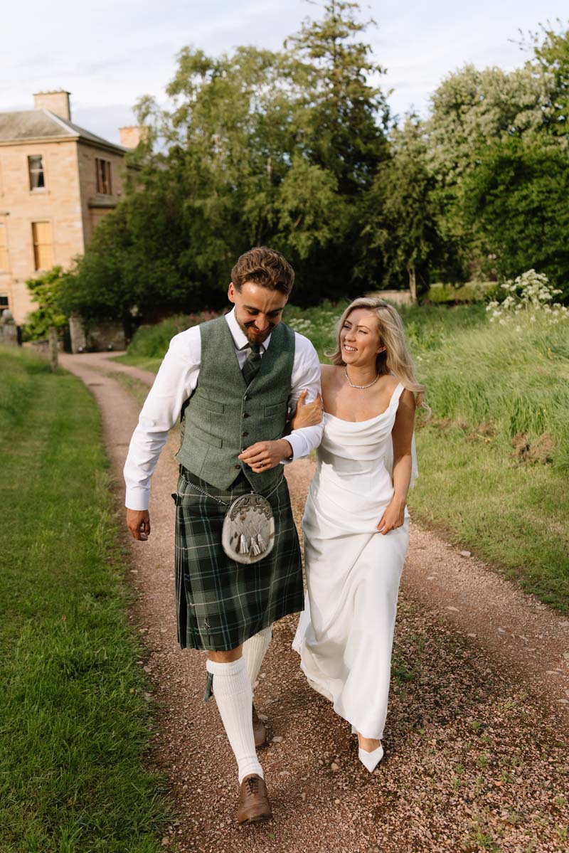 Newlyweds Lia and Louis walk together through the grounds of Cambo House following their Fife wedding ceremony.