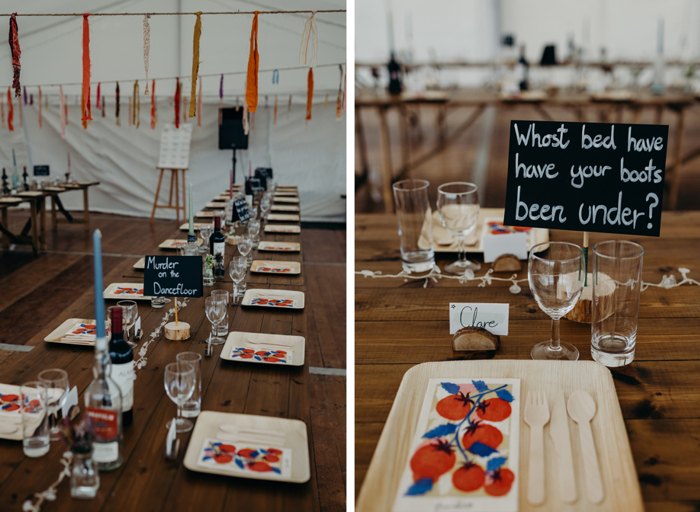 details of a table setting in a marquee featuring graphic red and blue tomato napkins, square wooden plates and cutlery. There is a wine glass and tall tumbler at each place setting and streamers in the background handing from the ceiling of a marquee