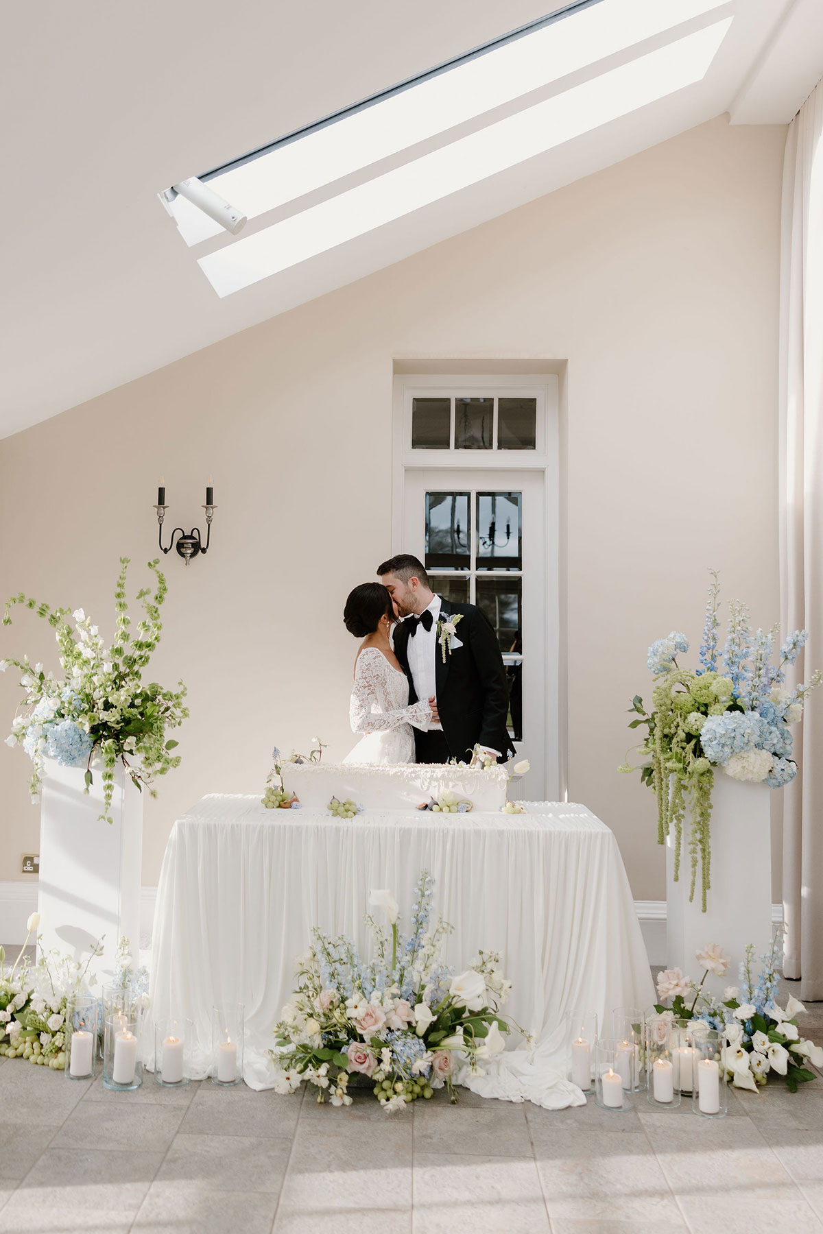 Bride and groom kissing behind a wedding cake framed by floral arrangements