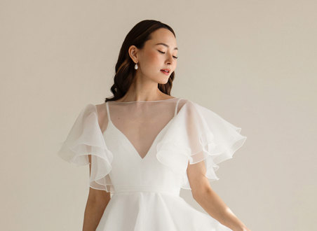 dark haired model wears v-neck white wedding dress with sheer layer over bodice providing fluttery sleeves