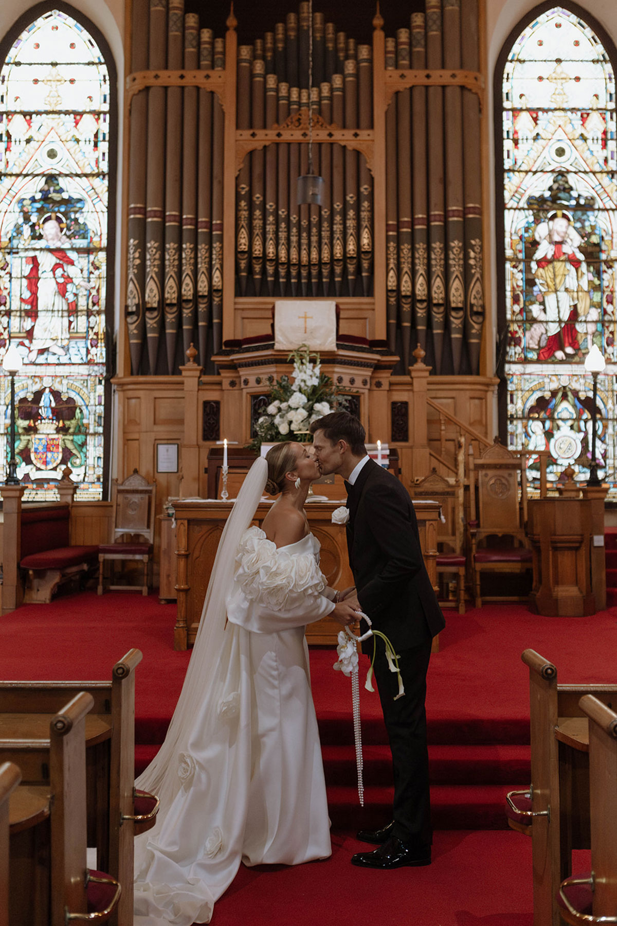 Bride and groom kissing at the altar in Kilwinning Abbey Church wedding ceremony, Ayrshire, with stained glass backdrop.