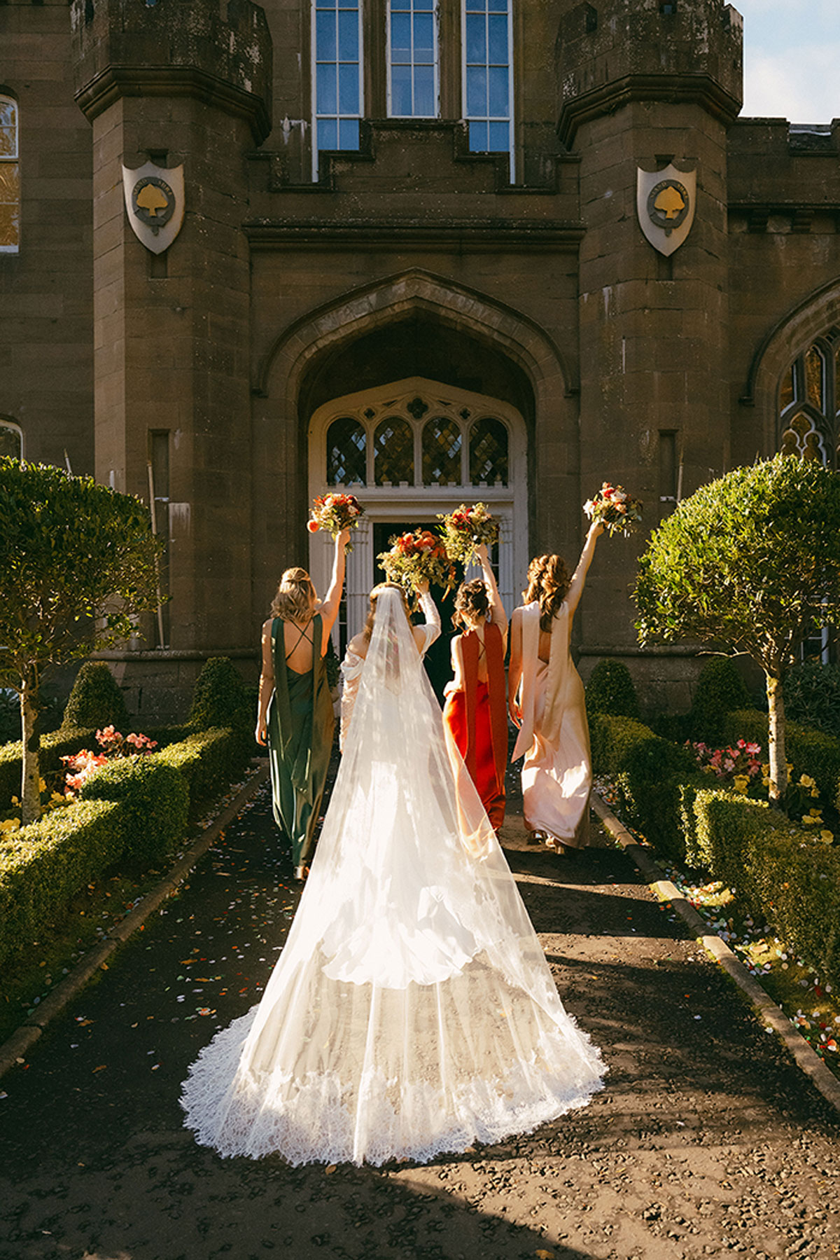 Bride and bridesmaids walking towards a Scottish castle wedding venue with bouquets raised