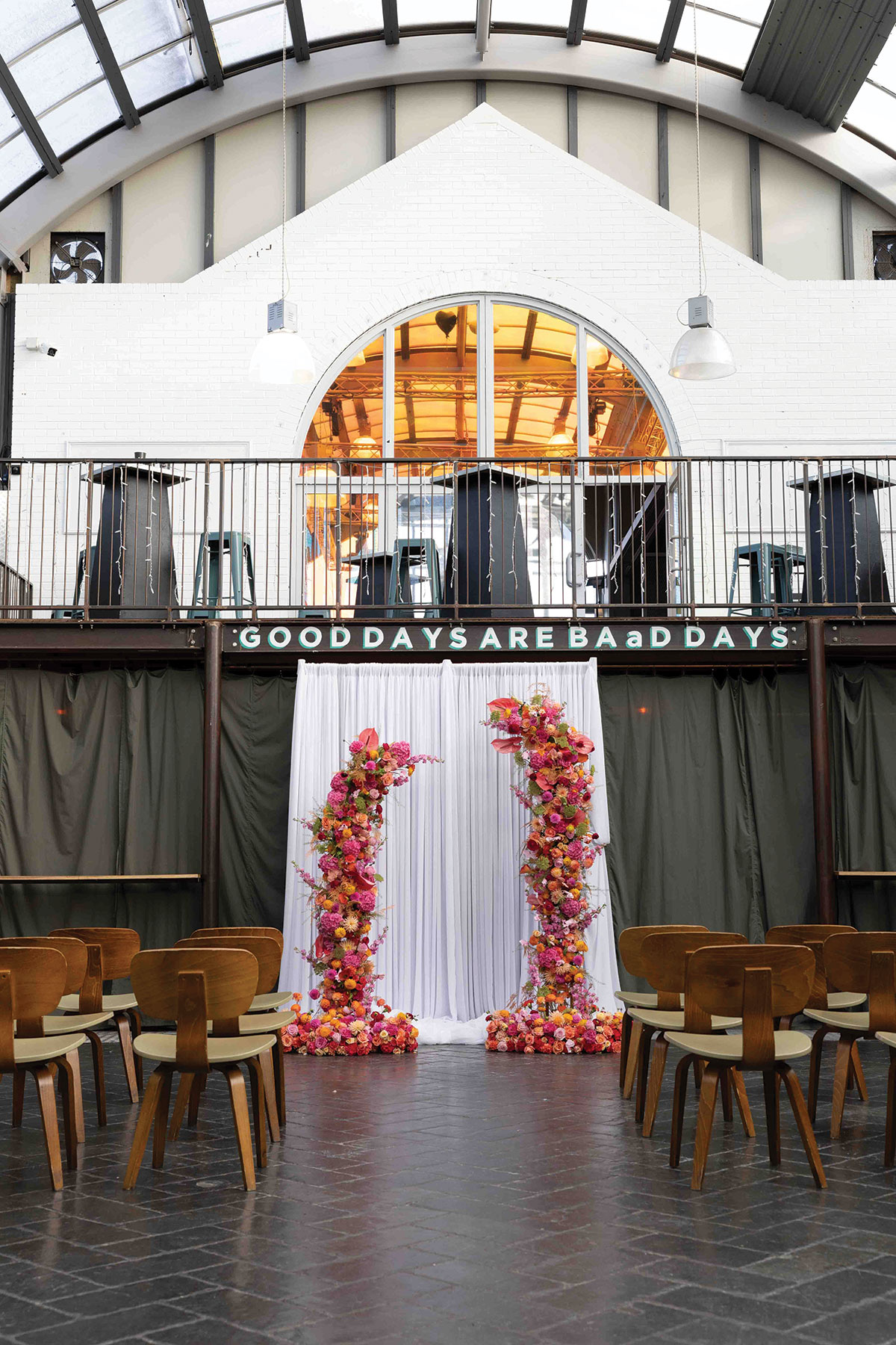 Industrial courtyard ceremony setup at BAaD Glasgow with colourful floral pillars and glass roof overhead