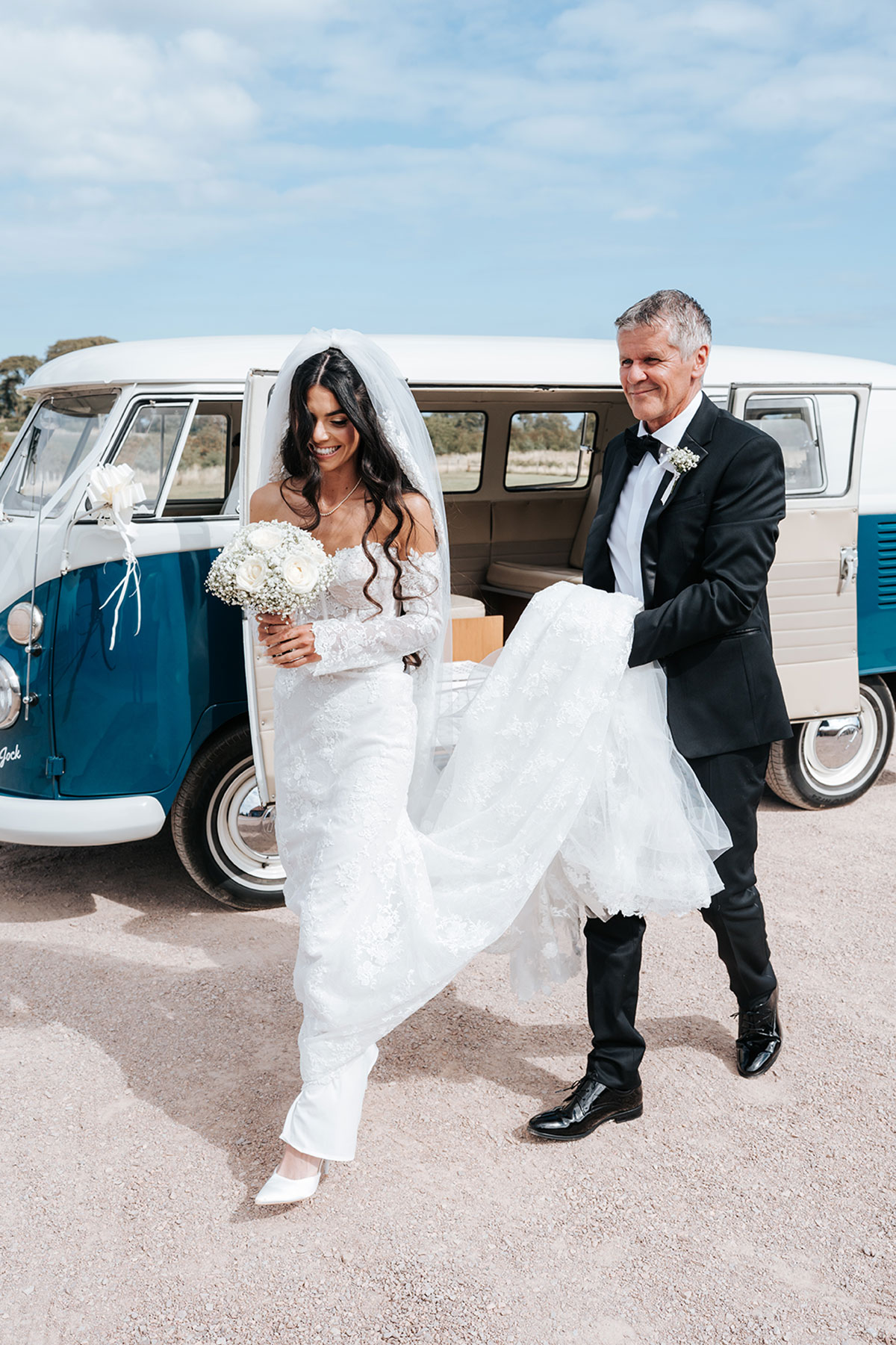 Bride stepping from a classic VW campervan, holding a white rose bouquet, ahead of the ceremony