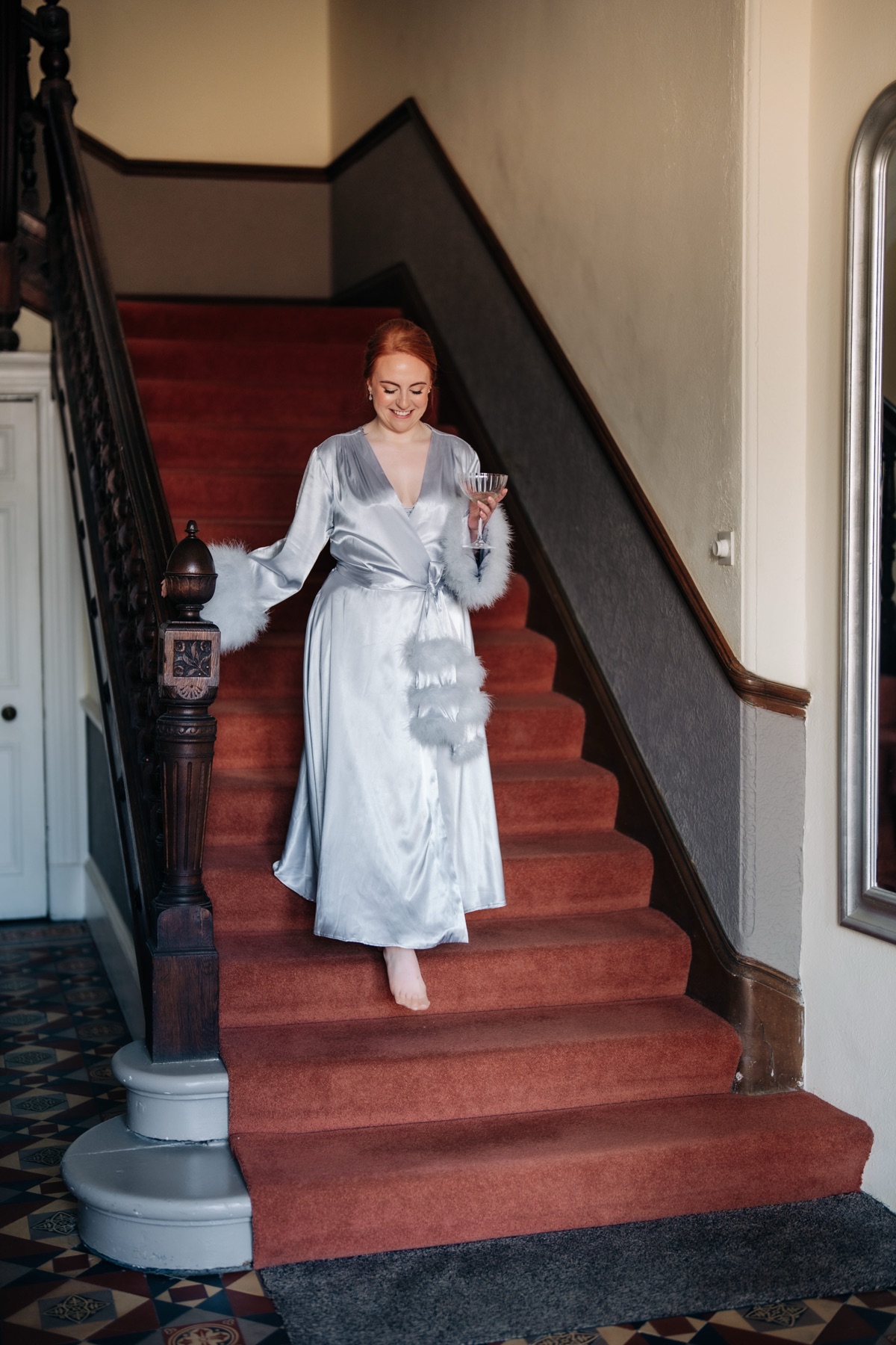 Robyn walks down a red-carpeted staircase in a pale blue satin bridal robe while getting ready for her Glasgow wedding.