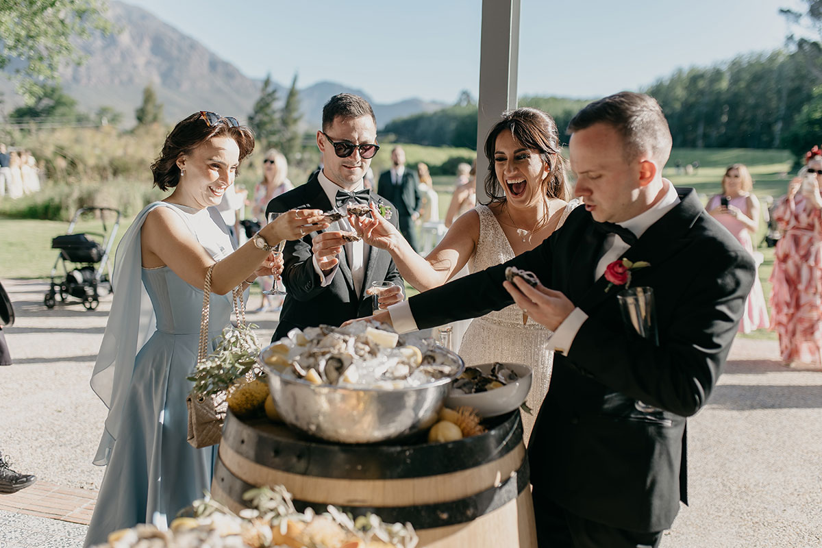 Newlyweds and wedding guests enjoying fresh oysters during drinks reception at Boschendal Wine Estate destination wedding