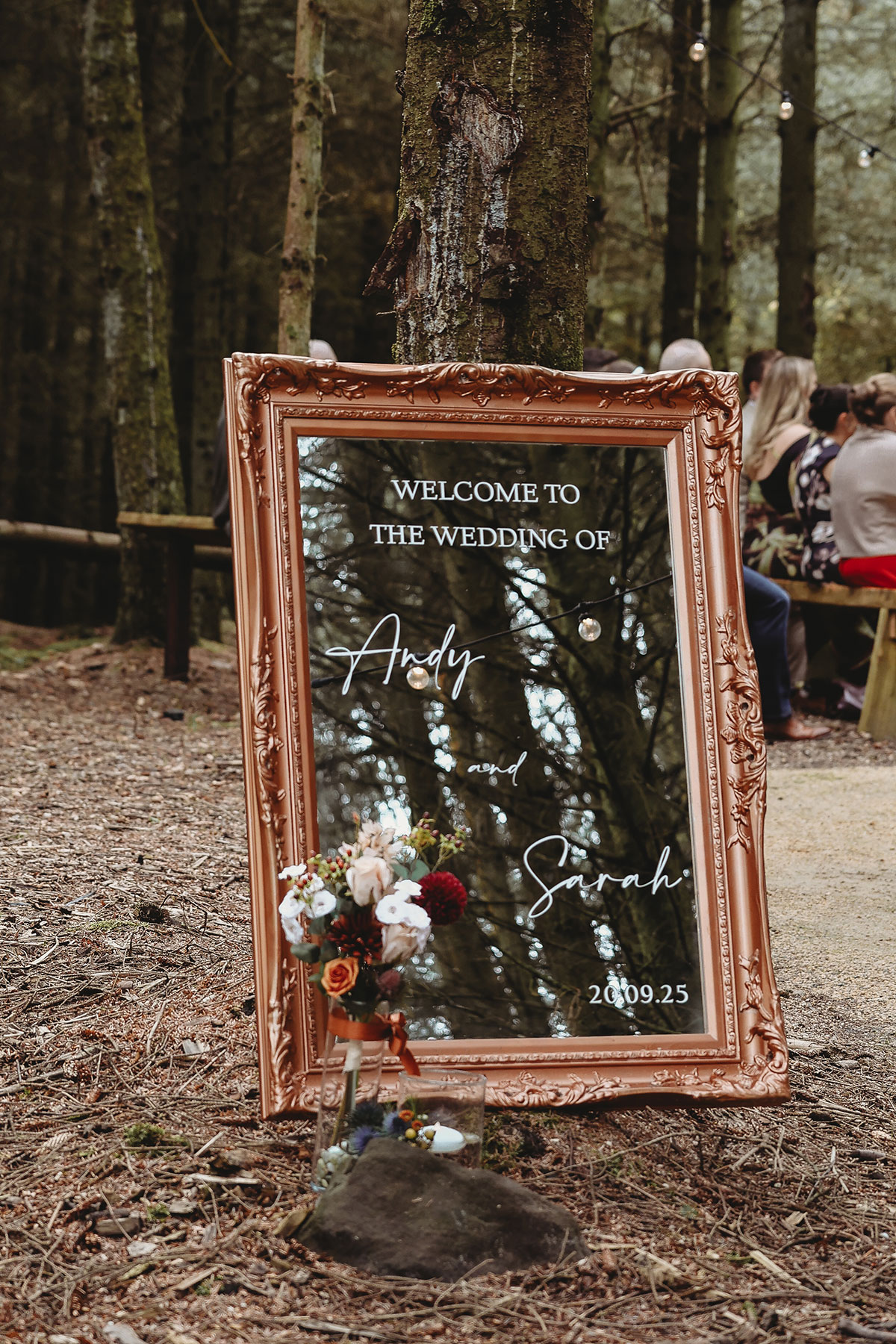Mirror welcome sign decorated with flowers at the entrance to an outdoor woodland wedding ceremony in Scotland