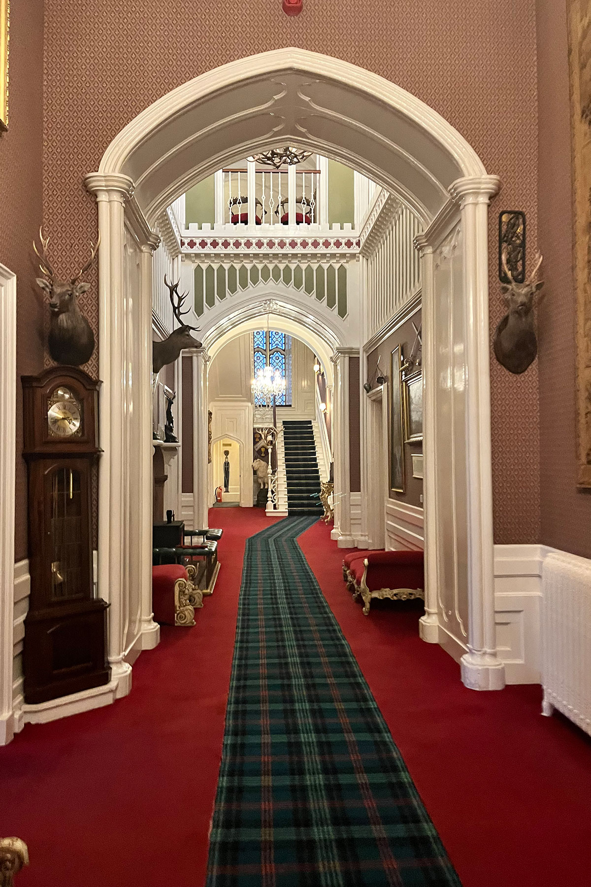 Elegant hallway inside a Scottish castle featuring tartan carpet, stag heads on the walls and a grand staircase with chandelier lighting
