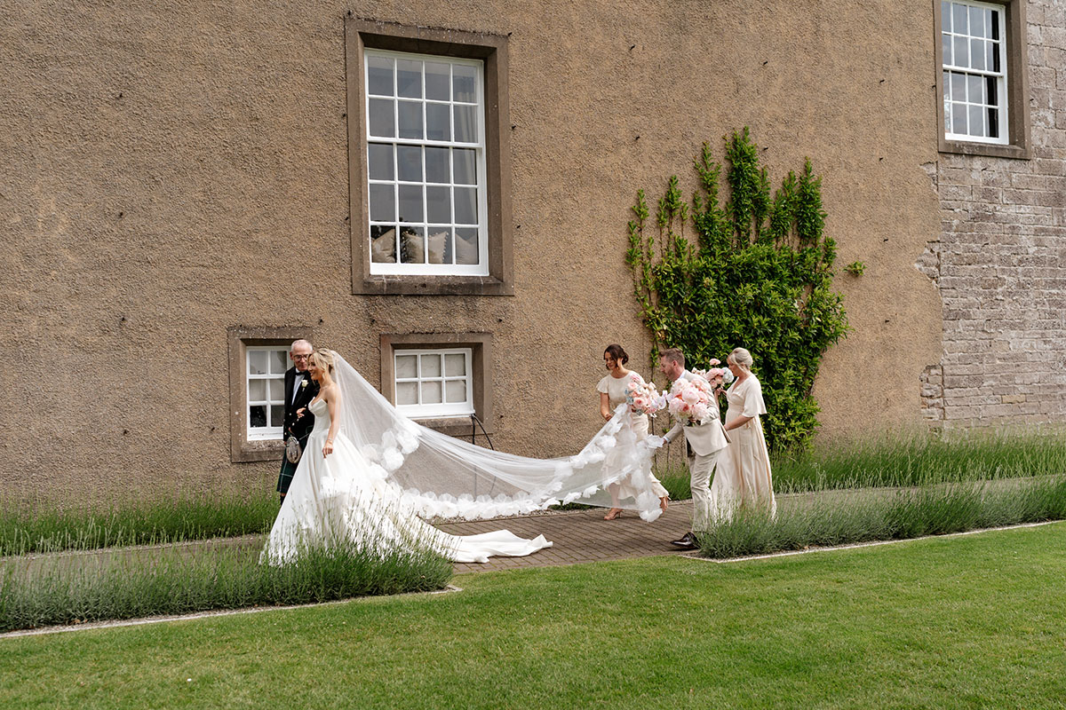 Bride walks with her father while bridesmaids and groomsmaid help carry her cathedral-length veil at Boturich Castle.