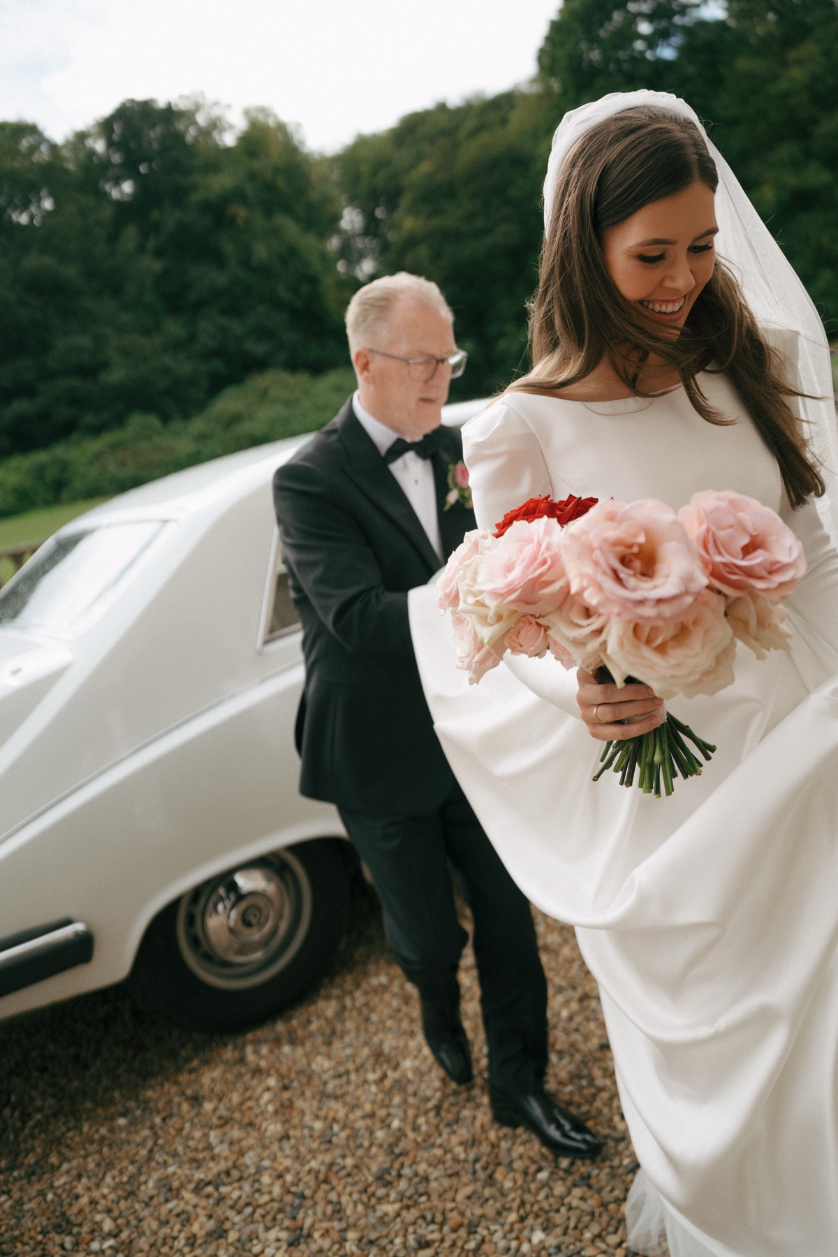 Bride Nicole arrives at Barnbougle Castle in South Queensferry with her dad, carrying a pink-and-red rose bouquet beside a vintage wedding car.