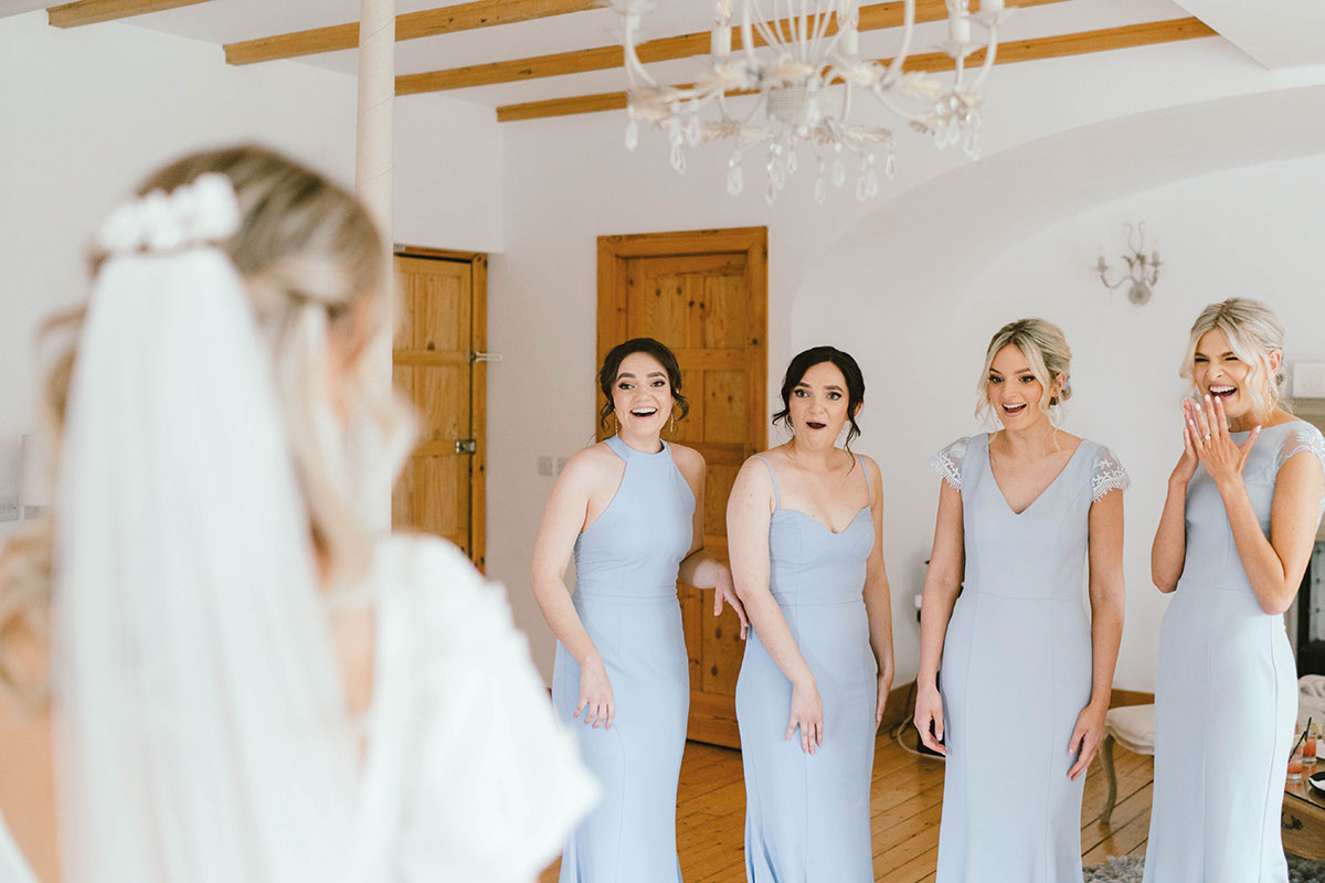 Bridesmaids in pale blue dresses reacting with excitement as they see the bride for the first time on the wedding morning.